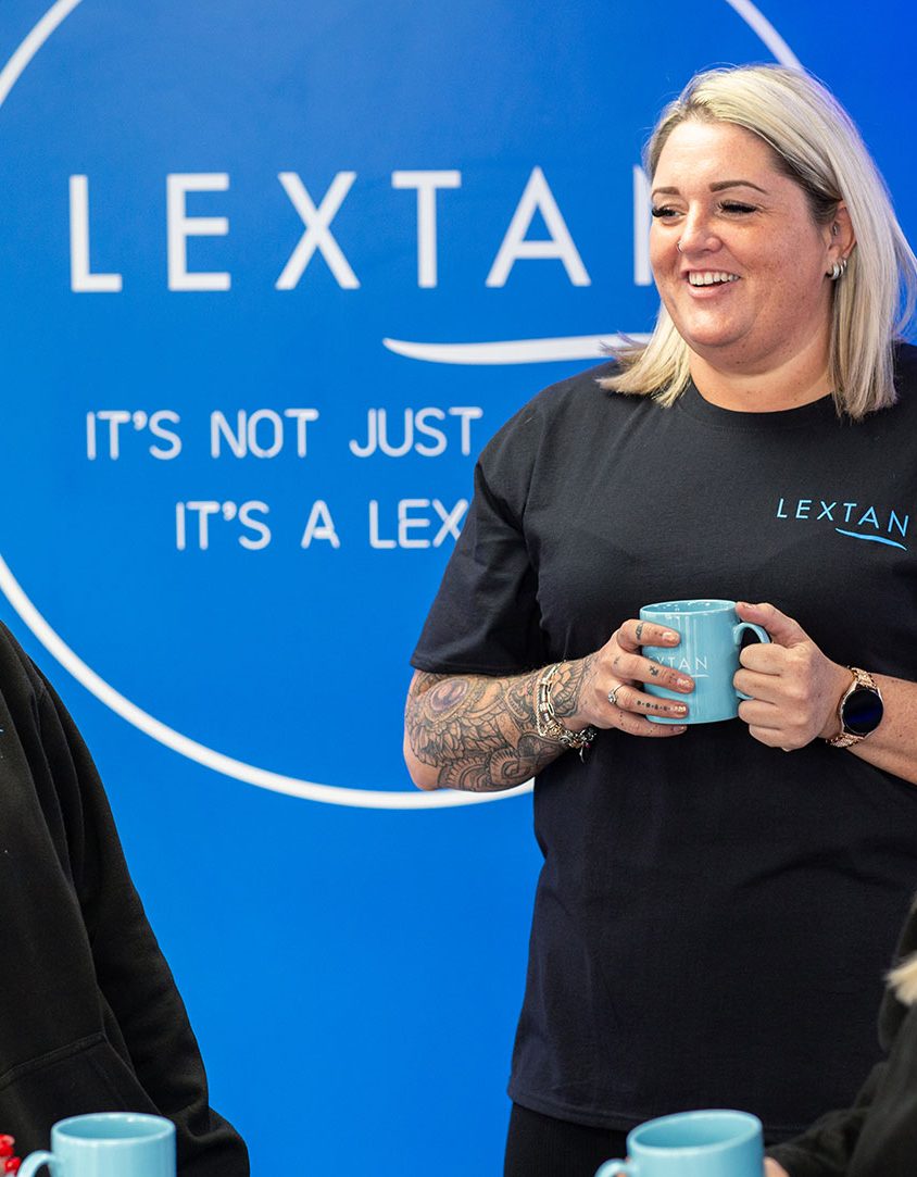 Three woman holding mugs in a lextan shop. 2 are sitting, one is standing.